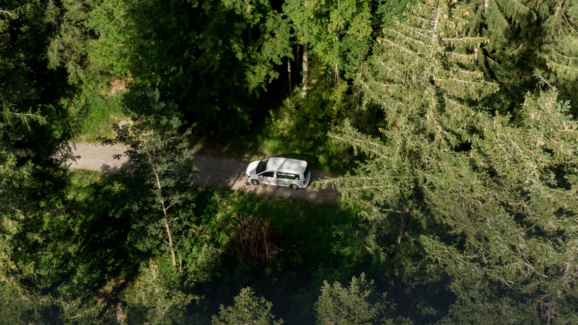Drohnenaufnahme eines ABT E-Caddy auf einem Feldweg im Wald
